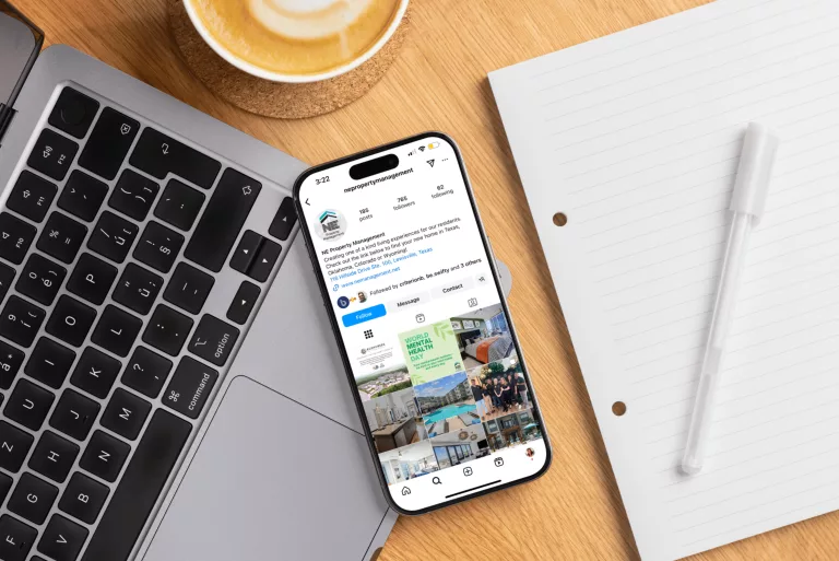 Laptop, phone showing an Instagram feed and a notebook on a wooden desk